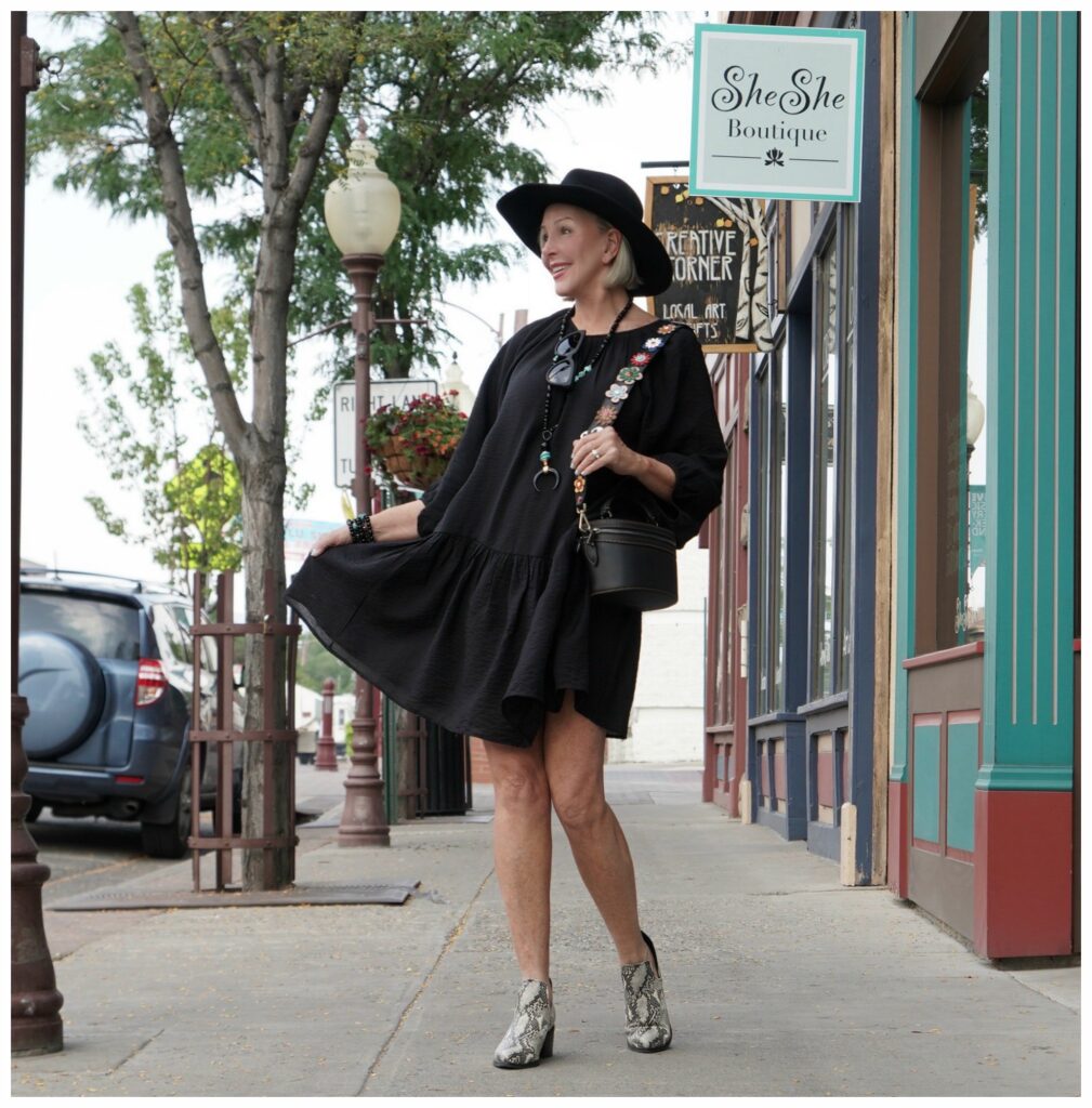 Sheree Frede of the SheShe Show standing in front of wood door wearing a knee length black dress