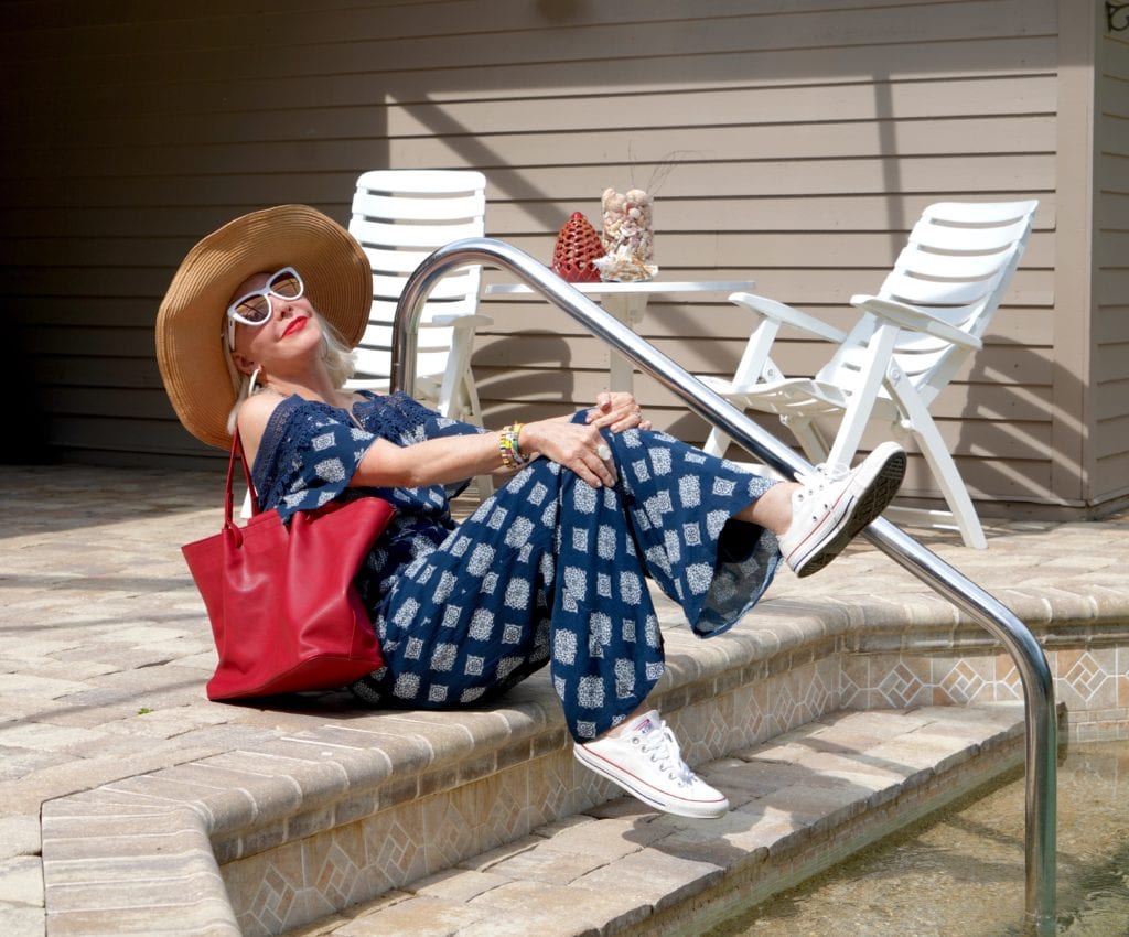navy print jumpsuit with ruffle off the shoulder, red tote bag white sneakers, wide brimmed hat and big sunglasses