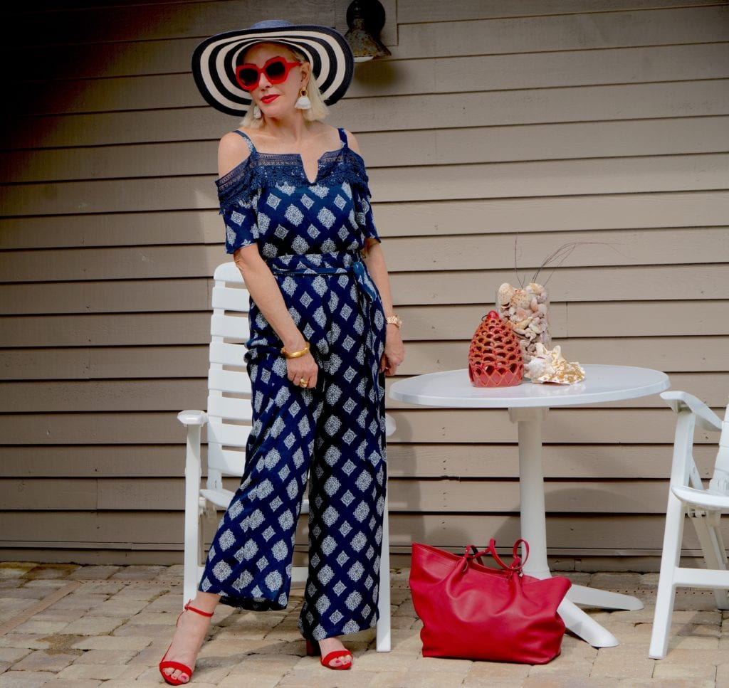navy print jumpsuit with ruffle off the shoulder, red tote bag white red heeled sandals, wide brimmed hat and big sunglasses