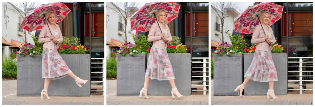 Sheree Frede standing in front of pretty spring flowers wearing a pink floral skirt and blush leather jacket and pink floral umbrella