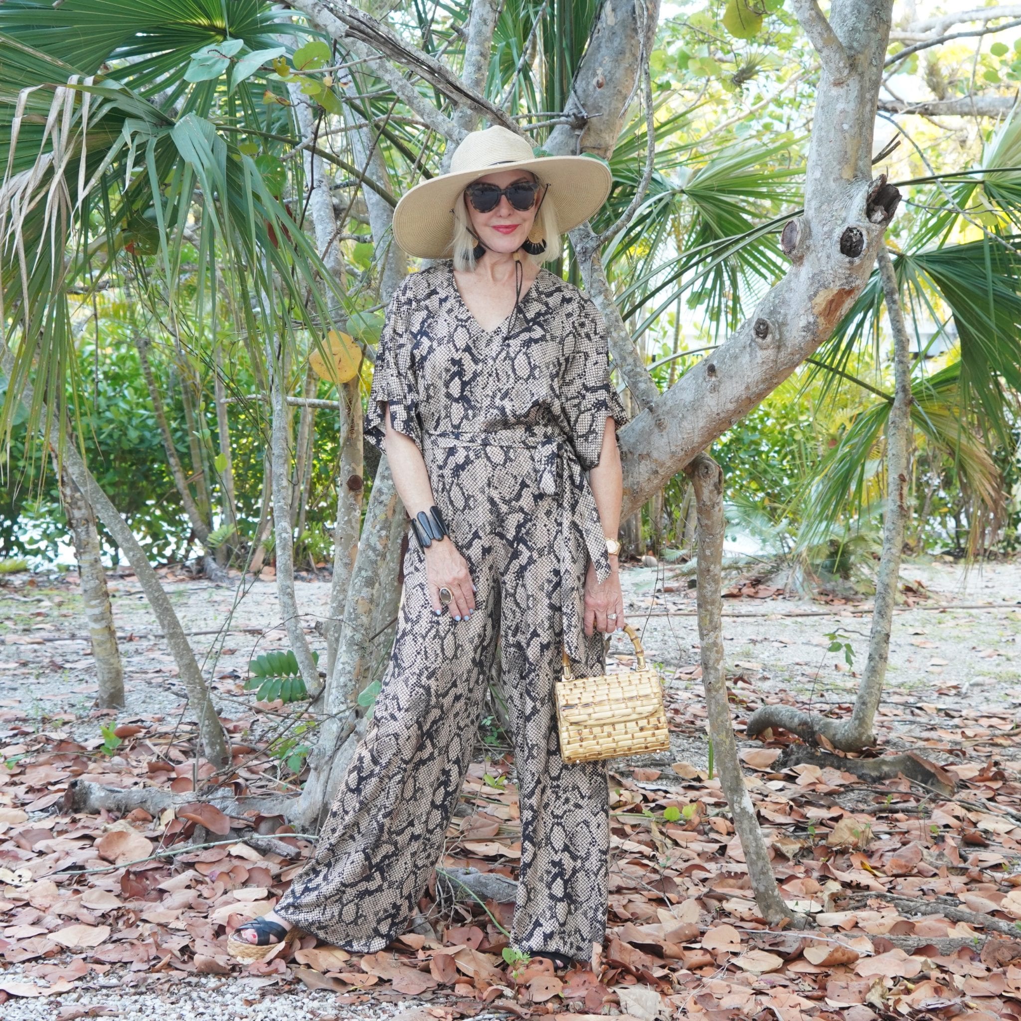 snakeskin print jumpsuit, bamboo bag, black wedge sandals, sunglasses, tropical setting
