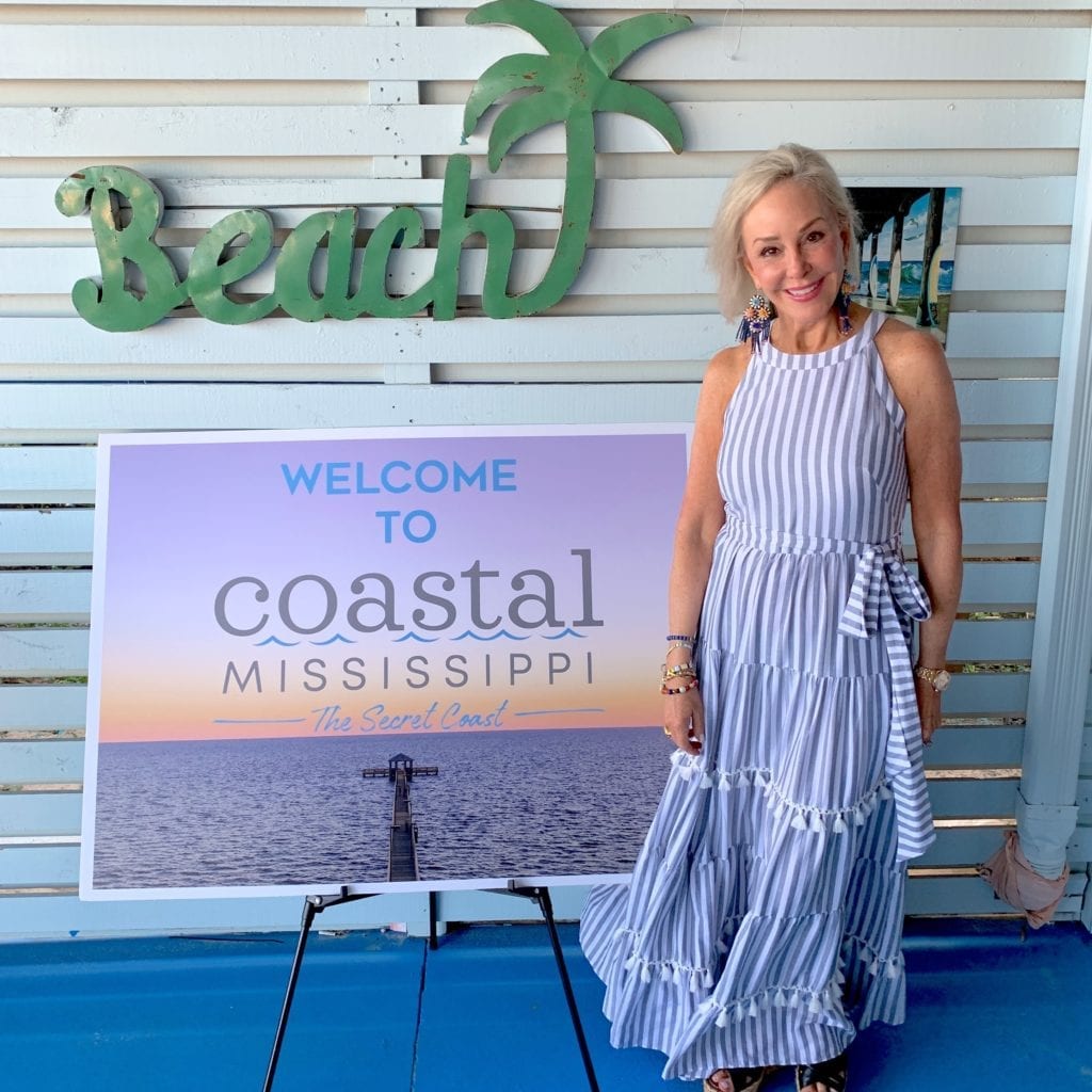 Sheree Frede of the SheShe Show wearing a blue dress by Coastal Mississippe sign