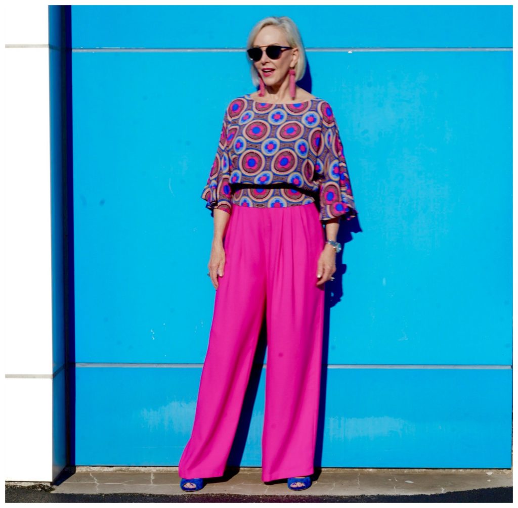 Sheree of the SheShe Show wearing hot pink wide leg pants and blue print top standing in front of blue wall