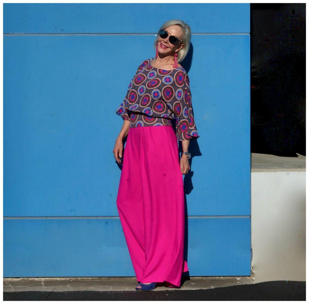 Sheree of the SheShe Show wearing hot pink wide leg pants and blue print top standing in front of blue wall