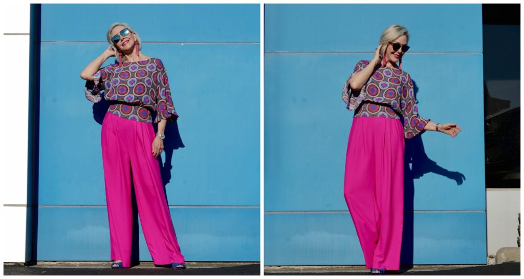 Sheree of the SheShe Show wearing hot pink wide leg pants and blue print top standing in front of blue wall