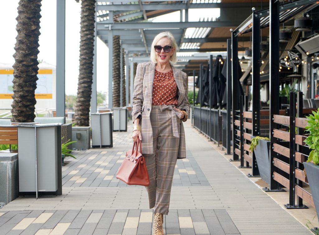 Sheree of the SheShe Show walking in front of outdoor mall wearing a plaid suit with rust with white polka dot tops and leopard booties