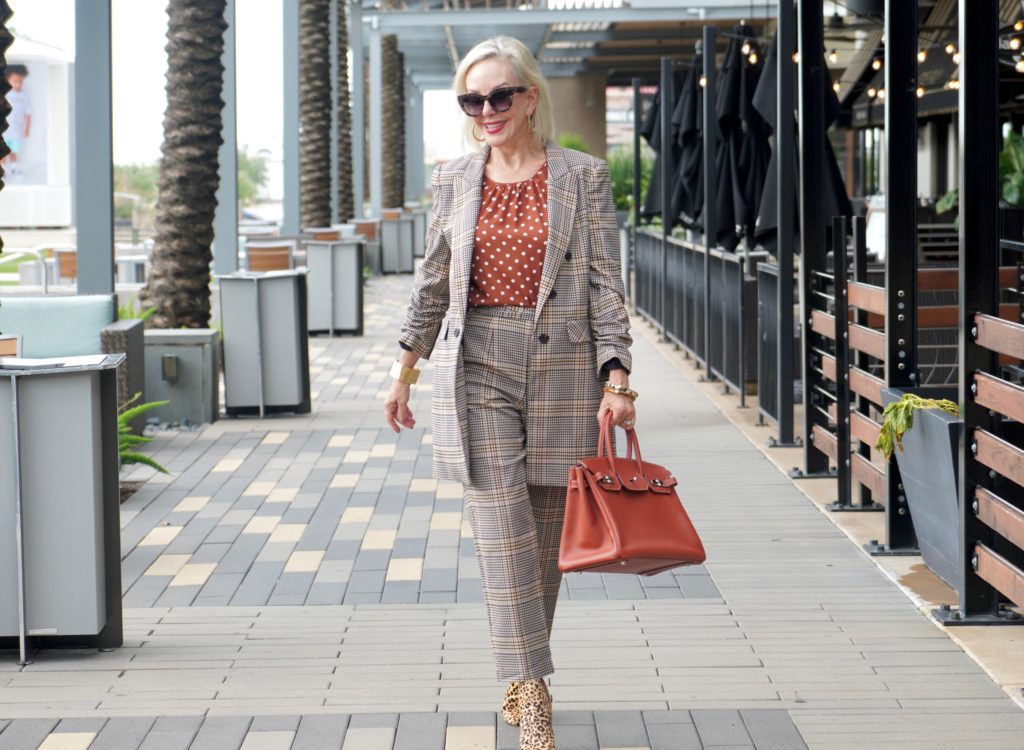 Sheree of the SheShe Show walking in front of outdoor mall wearing a plaid suit with rust with white polka dot tops and leopard booties