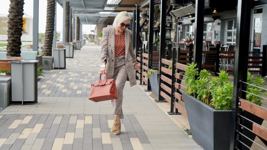 Sheree of the SheShe Show walking in front of outdoor mall wearing a plaid suit with rust with white polka dot tops and leopard booties