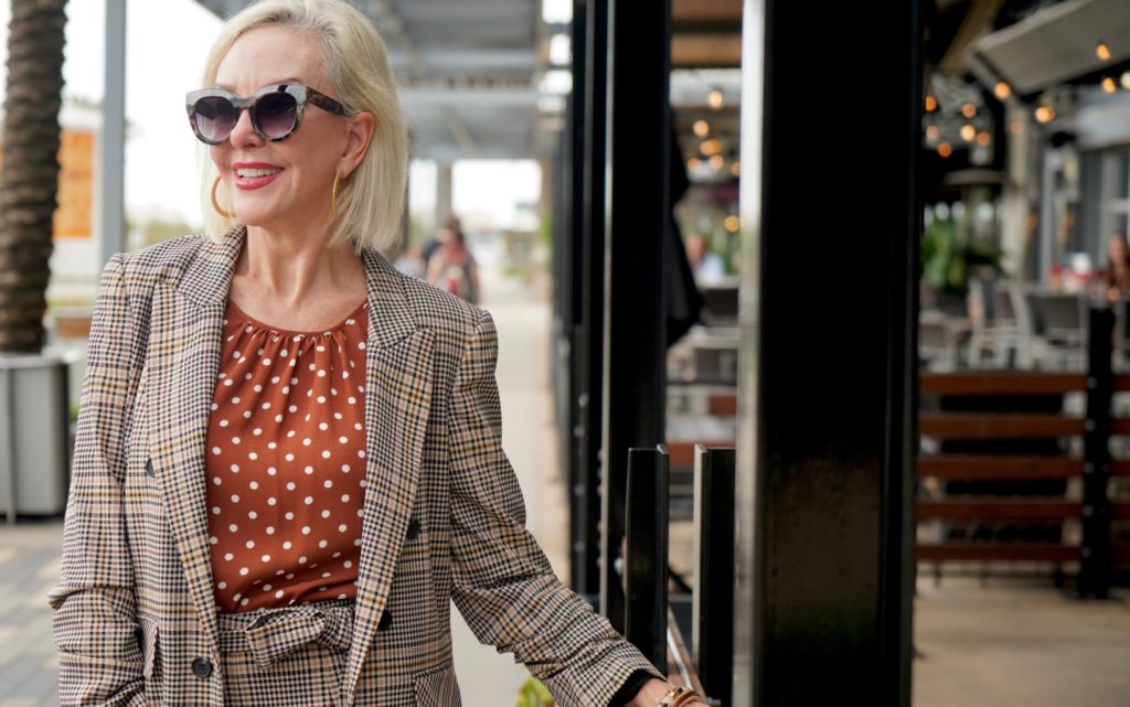 Sheree of the SheShe Show walking in front of outdoor mall wearing a plaid suit with rust with white polka dot tops and leopard booties