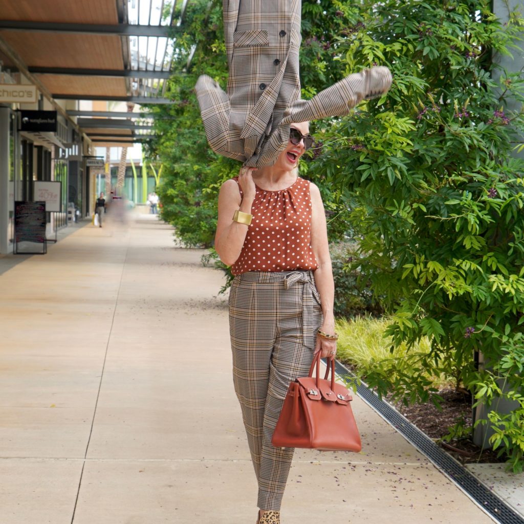 Sheree of the SheShe Show walking in front of outdoor mall wearing a plaid suit with rust with white polka dot tops and leopard booties