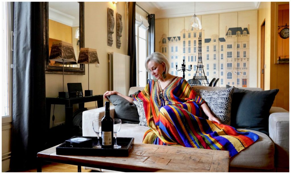 SheShe of the SheSheShow wearing a rainbow colored kimono lounging on a sofa at  Paris Perfect apartment rentals