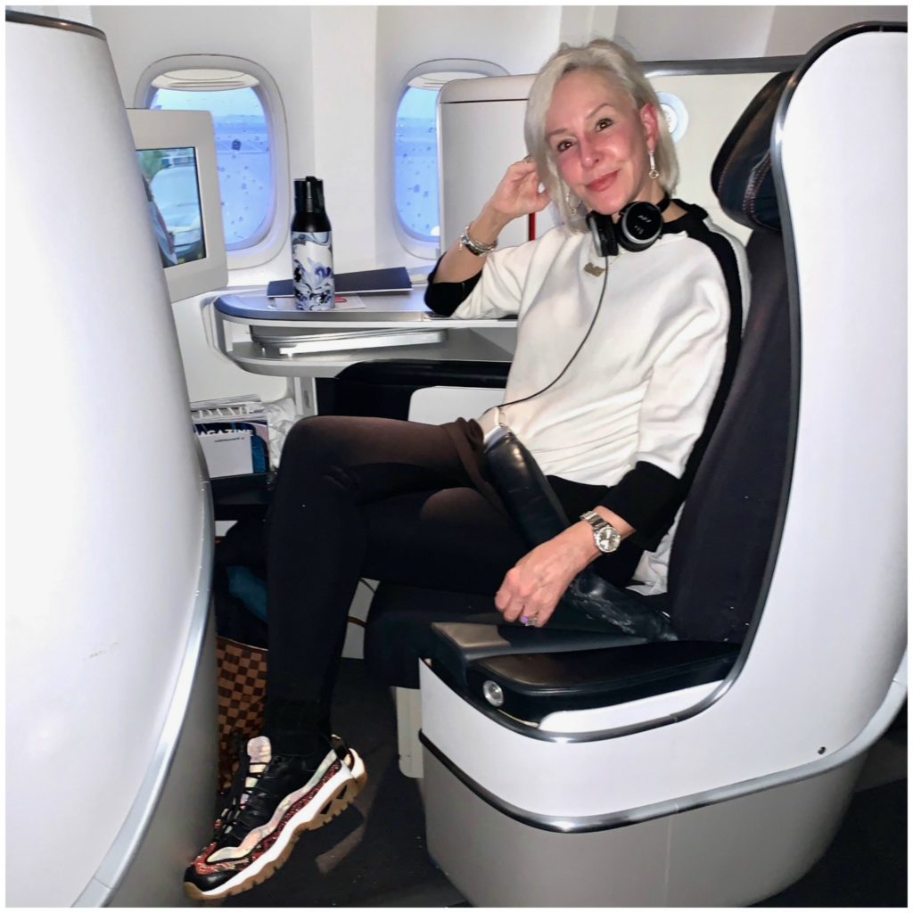 Sherere of the SheShe Show sitting in Air France Business First wearing white top with black leggings and sneakers