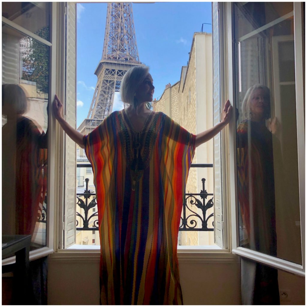 Sheree of the SheShe Show standing at window with Eiffel Tower in the background wearing a colorful stripe Kimono