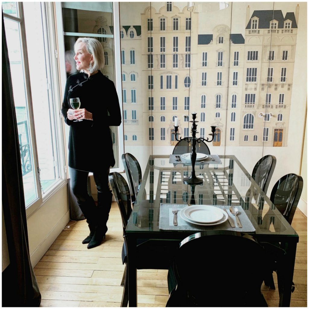 Sheree of the SheShe Show standing at window in dining room apartment in Paris wearing a black tunic and leggings