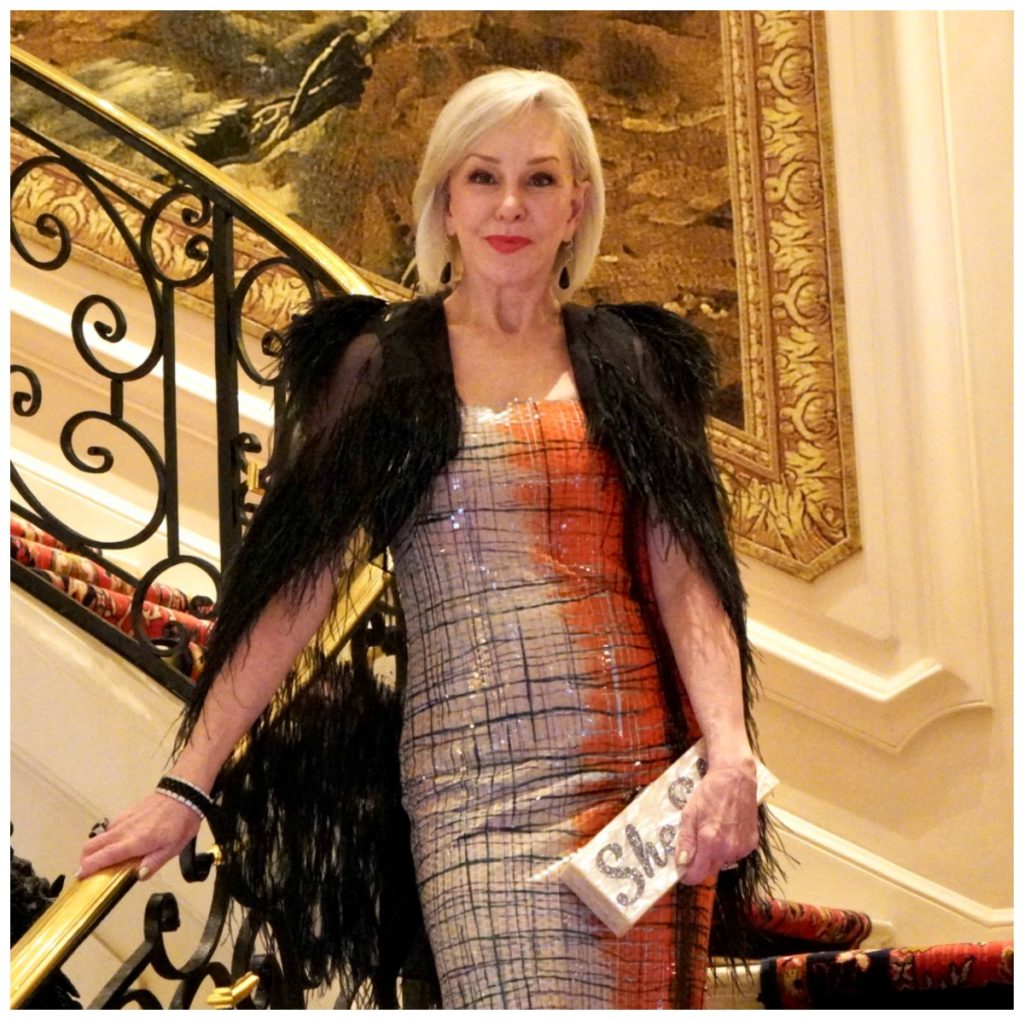 Sheree of the SheShe Show standing on grand staircase wearing an orange sequin gown and black mesh caplet