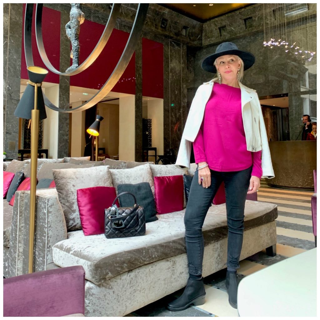 Sheree of te SheSheShow wearing fucshia top, white leather moto jacket, gray jeans and black hat