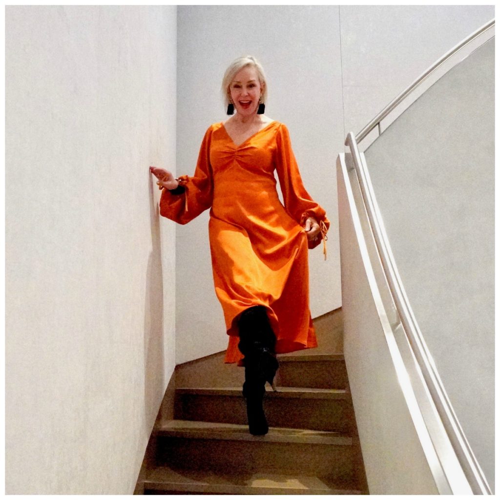 Sheree of sheshe show wearing an orange satin midi dress on stairs