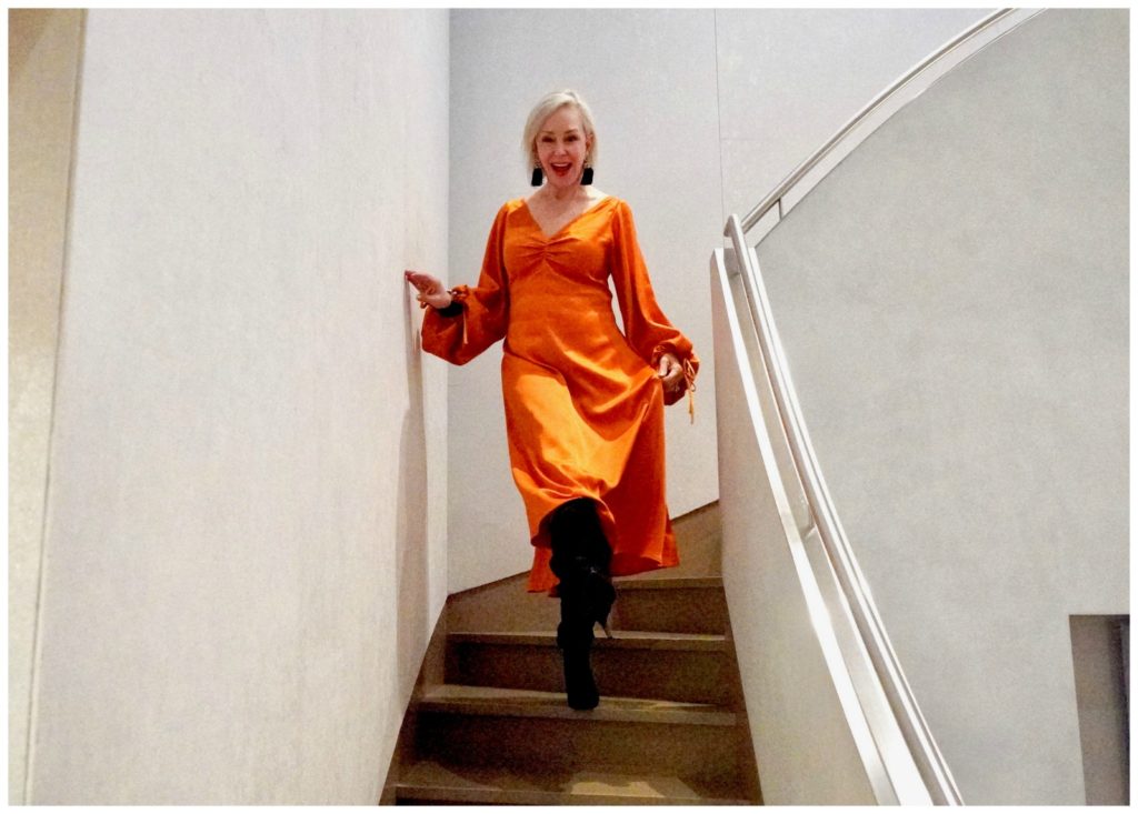 Sheree of the SheShe Show coming down stairs wearing orange satin dress