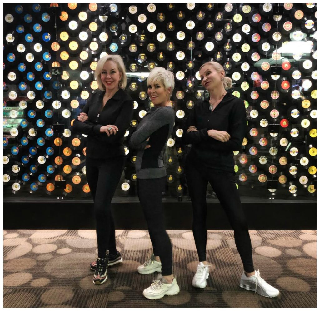 Sheree, Shauna & Jamie wearing black athleisure wear standing in front of a wall of 45 records