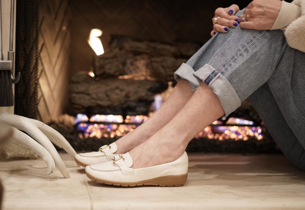 Legs wearing white loafers and jeans in front of a fireplac