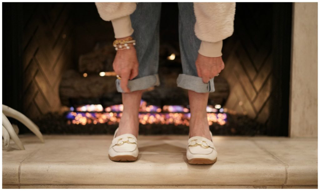 Legs wearing white loafers and jeans in front of a fireplac