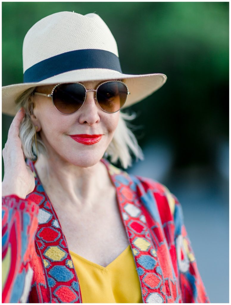 Sheree of the SheSheShow walking on wood walking bridge wearing a red print duster with yellow camisole. Panama hat