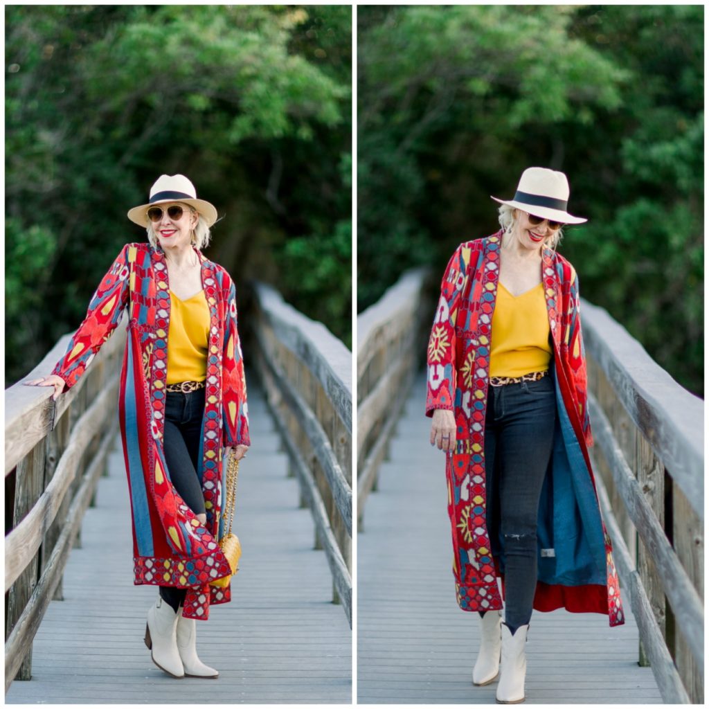 Sheree of the SheSheShow walking on wood walking bridge wearing a red print duster over blue jeans and yellow camisole. Panama hat