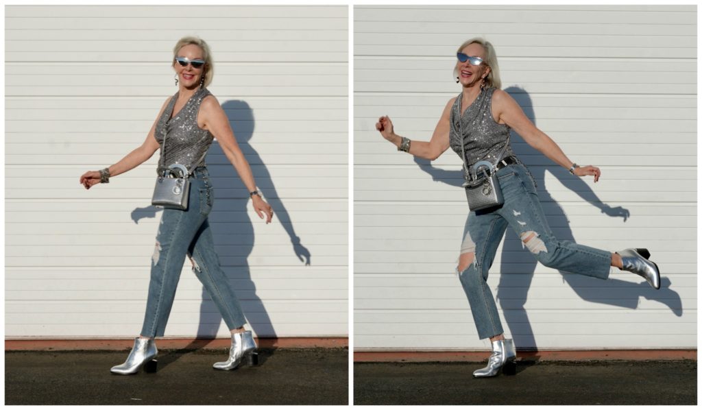 Sheree Frede of the SheShe Show walking in front of a white wall wearing gray sequin cowl neck top by Eliza J with ripped denim jean and silver booties