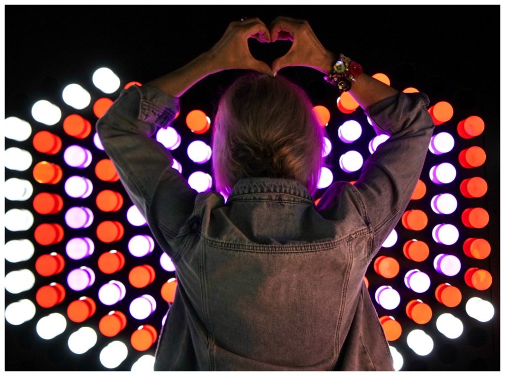 Night lights behind Sheree Frede's back. Heart sign with hand over head