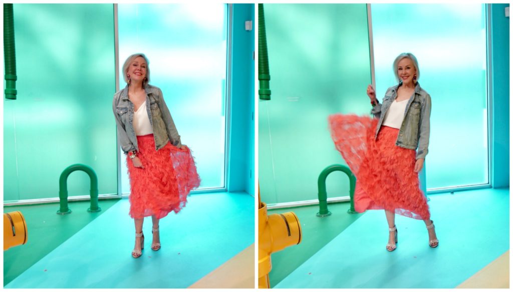 Sheree Frede of the SheShe Show wearing a bright coral midi length skirt, denim jacket over white camisole and rhinestone shoes swishing her skirt