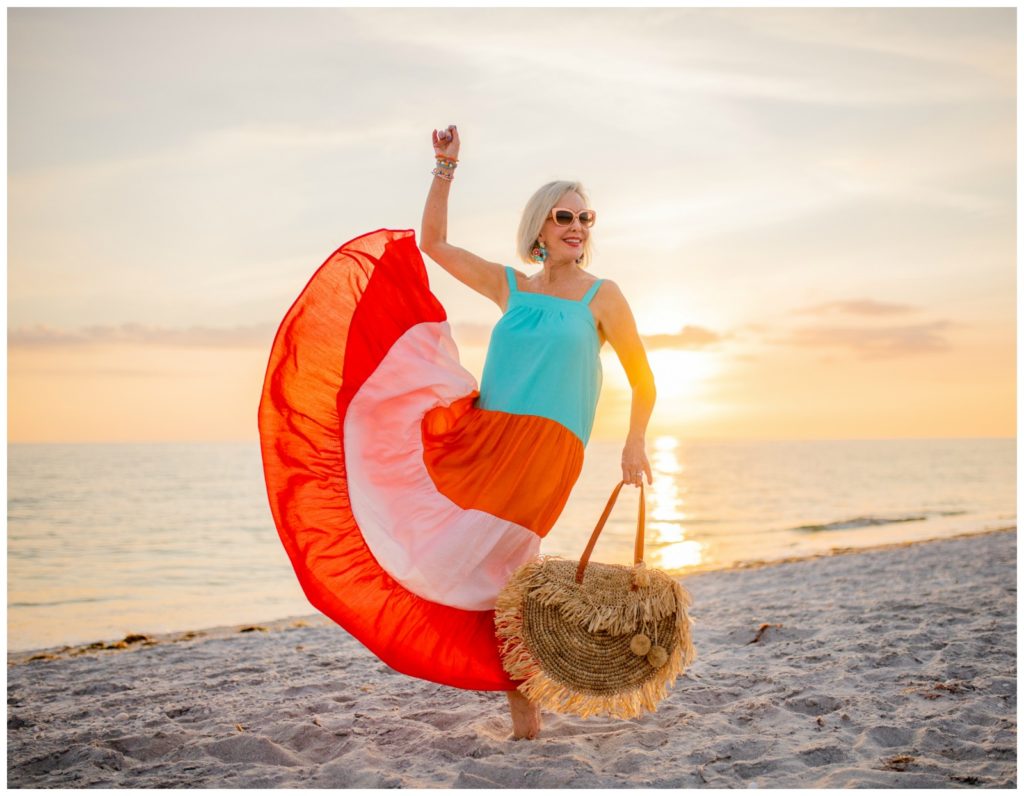 Sheree Frede of the SheShe Show on the beach at sunset wearing a orange and turquoise maxi dress