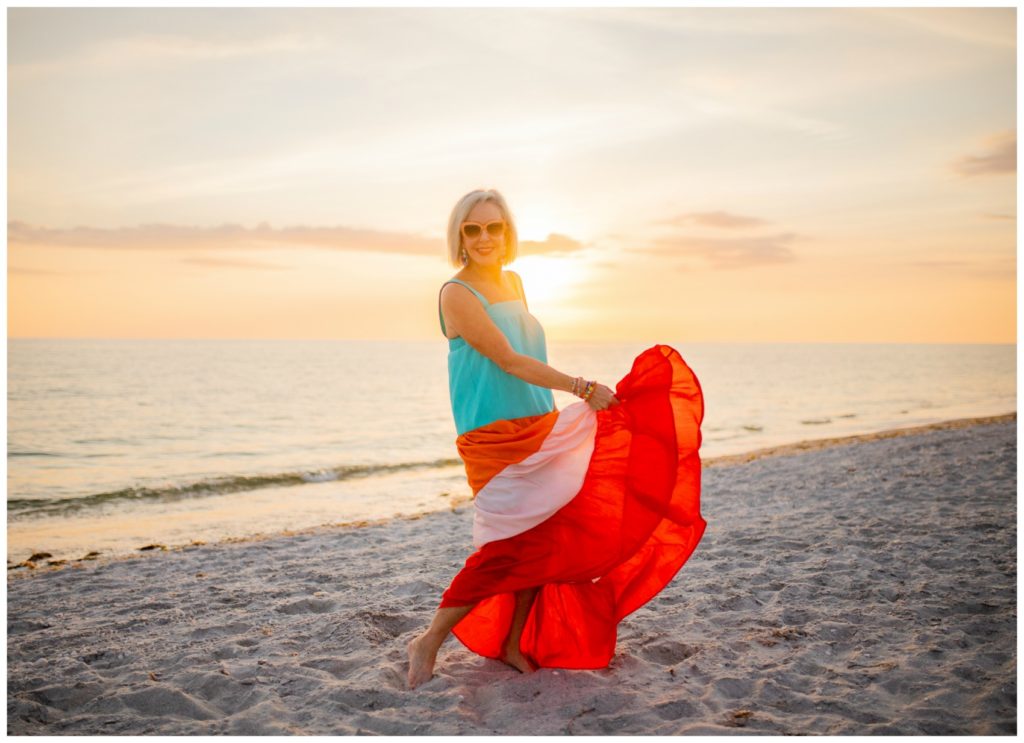 Sheree Frede of the SheShe Show on the beach at sunset wearing a orange and turquoise maxi dress