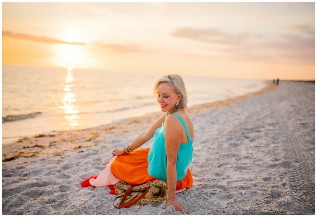 Sheree Frede of the SheShe Show on the beach at sunset wearing a orange and turquoise maxi dress