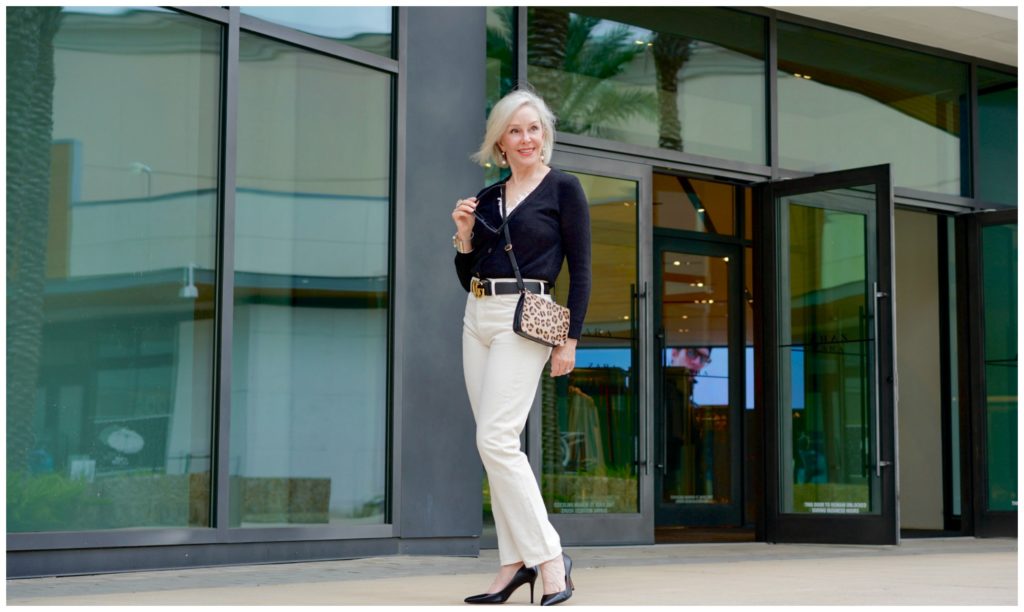 Sheree Frede of the SheShe Show standing in front of a store front  wearing off white jeans and black sweater. 