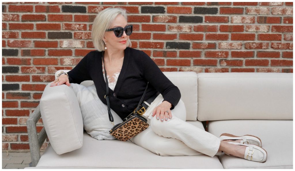 Sheree Frede of the SheShe Show sitting on a big offwhite sofa wearing off white jeans and black sweater.