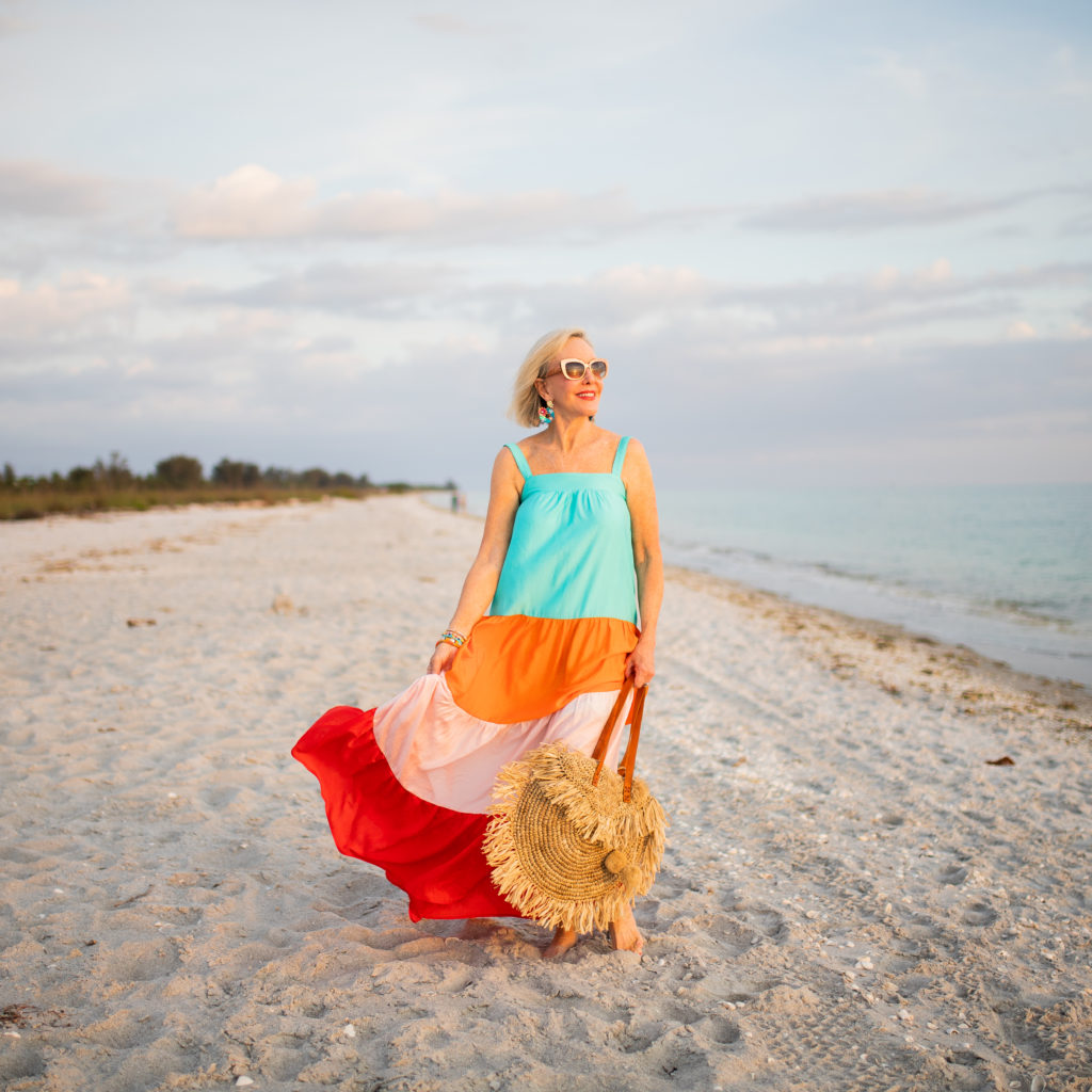 Sheree Frede of the SheShe Show on the beach at sunset wearing a orange and turquoise maxi dress