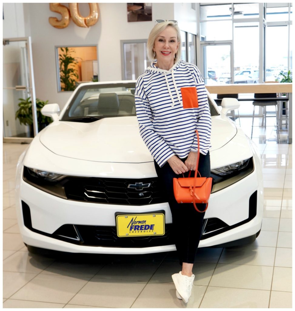 Sheree Frede standing in front of white Chevrolet wearing white and blue stripes with orange pocket