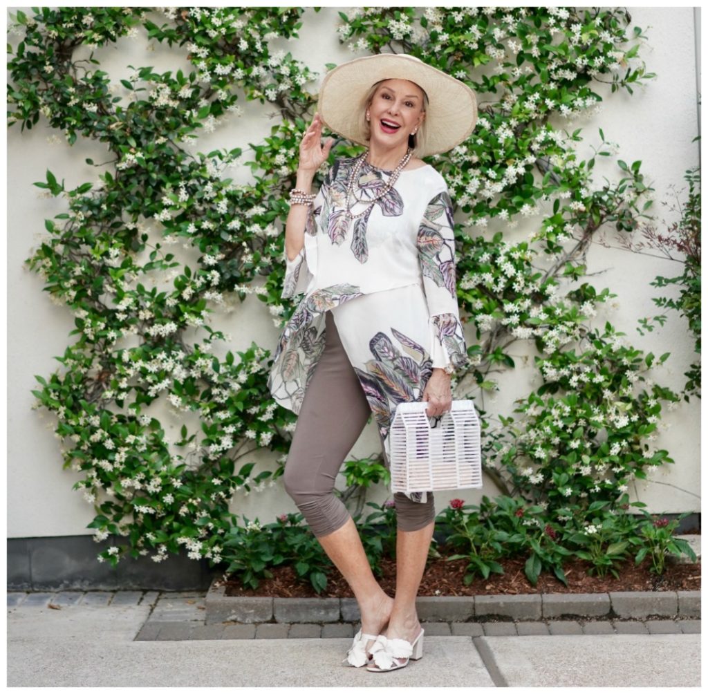 Sheree Frede of the SheShe Show standing in front of jasmine vine wall wearing print top over leggings