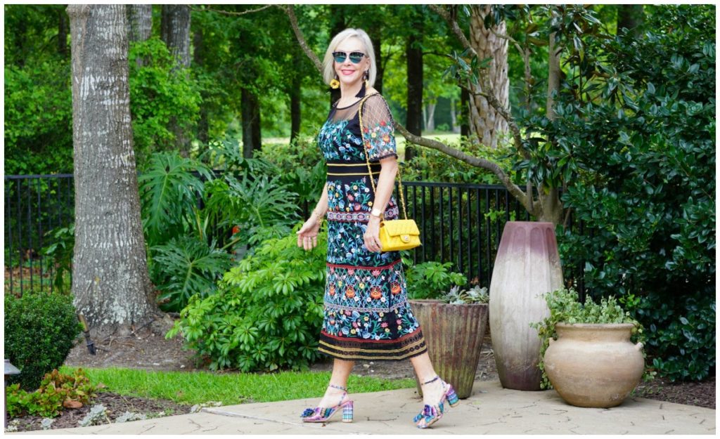 Sheree Frede of the SheShe Show standing by swimming pool wearing sunglasses and a black floral dress