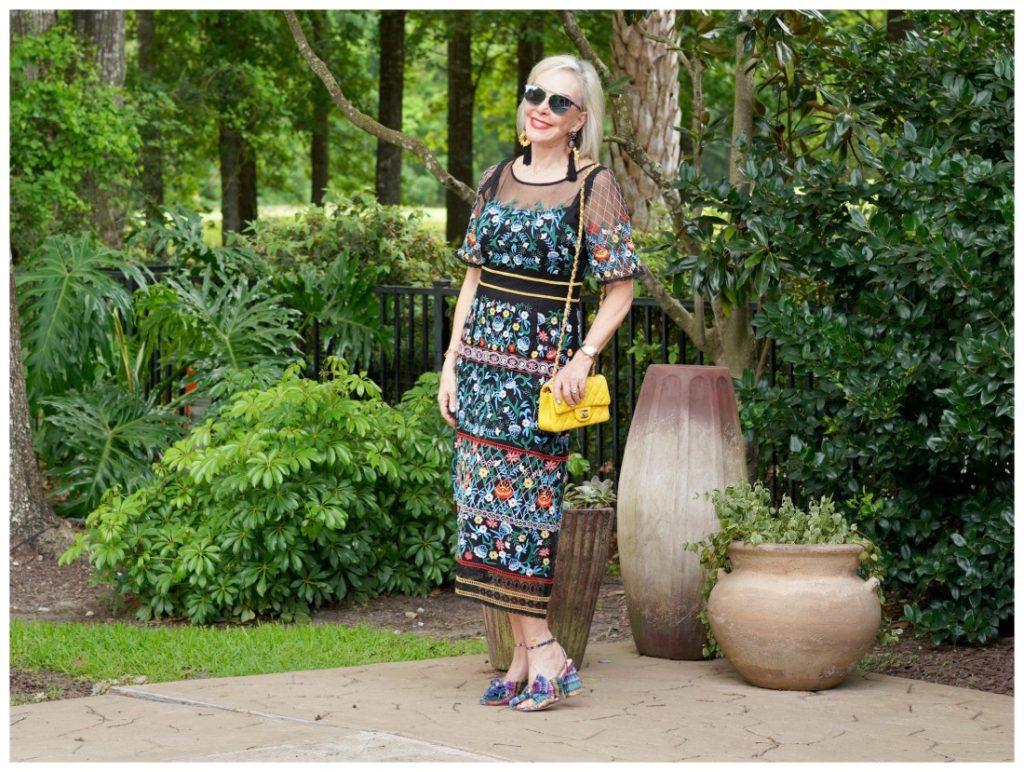 Sheree Frede of the SheShe Show standing by swimming pool wearing sunglasses and a black floral dress