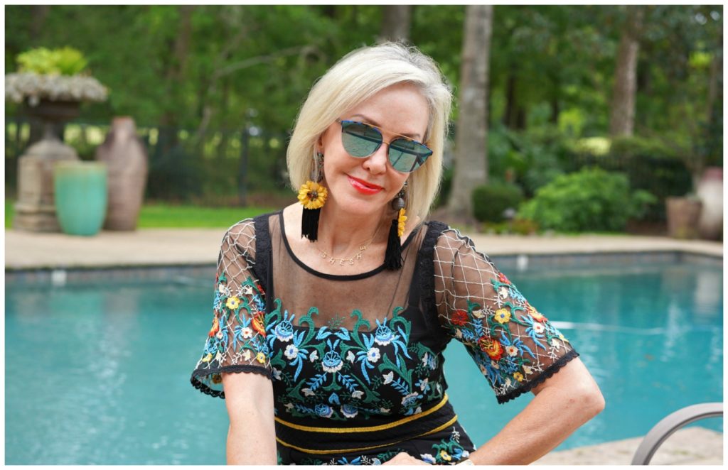 Sheree Frede of the SheShe Show sitting by swimming pool wearing sunglasses and a black floral dress