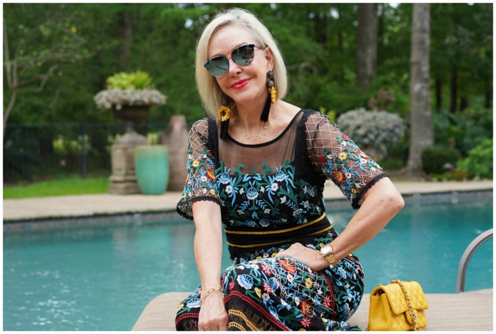 Sheree Frede of the SheShe Show sitting by swimming pool wearing sunglasses and a black floral dress