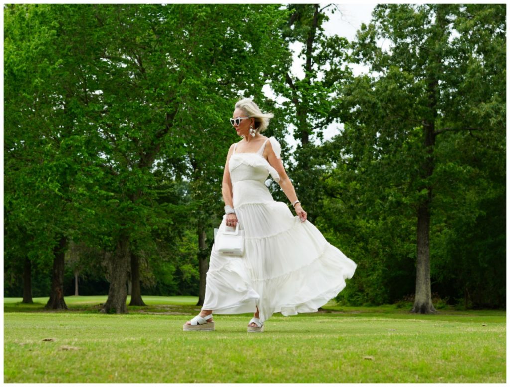 Sheree Frede of the SheShe Show wearing a white flowy maxi dress on a green lawn and wooded background