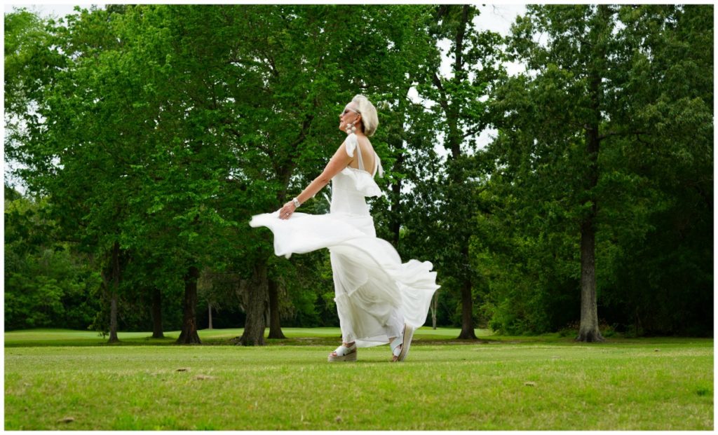 Sheree Frede of the SheShe Show wearing a white flowy maxi dress on a green lawn and wooded background