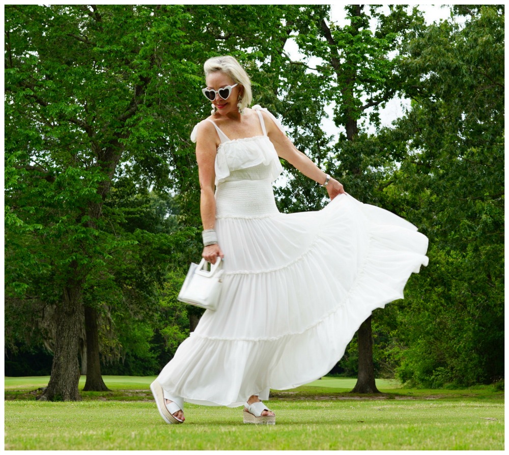 Sheree Frede of the SheShe Show wearing a white flowy maxi dress on a green lawn and wooded background