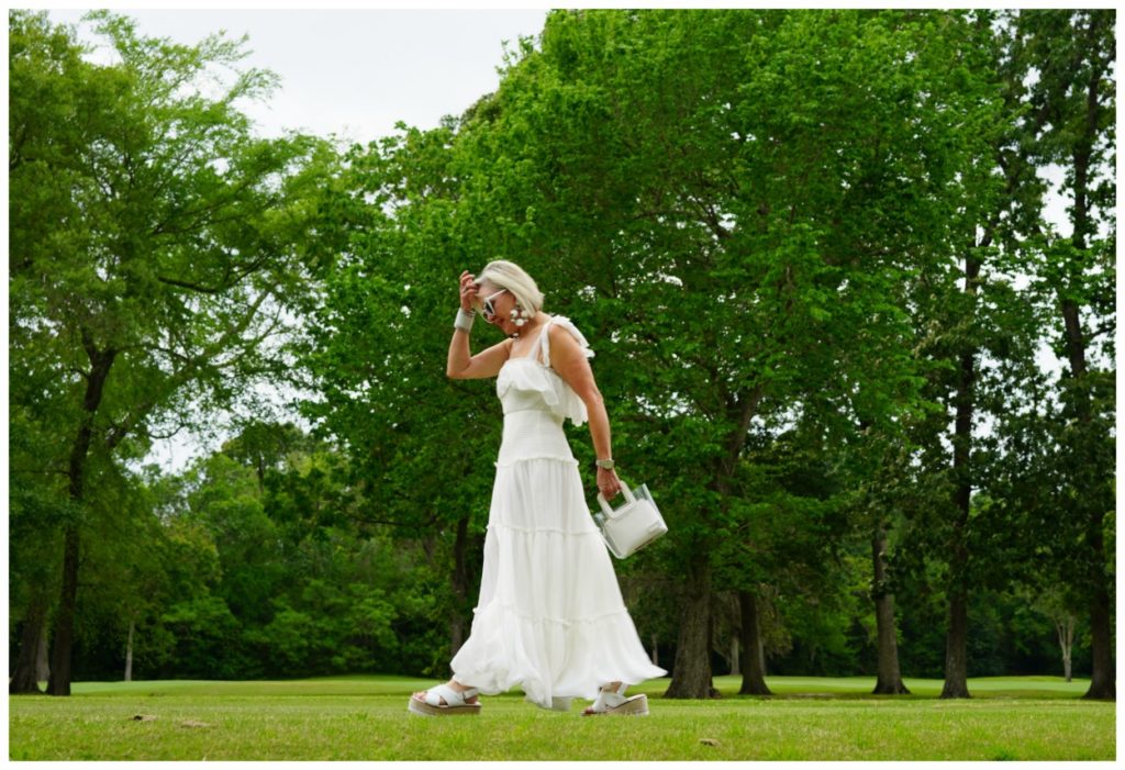 Sheree Frede of the SheShe Show wearing a white flowy maxi dress on a green lawn and wooded background