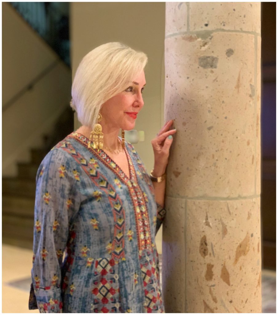 Sheree Frede of the SheShe Show standing in foyer by column wearing a chambray maxi dress accented in embellishments