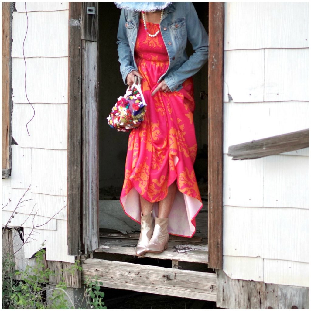 Sheree Frede of the SheShe Who standing in an abandoned house wearing an orange and pink maxi dress with denim jacket