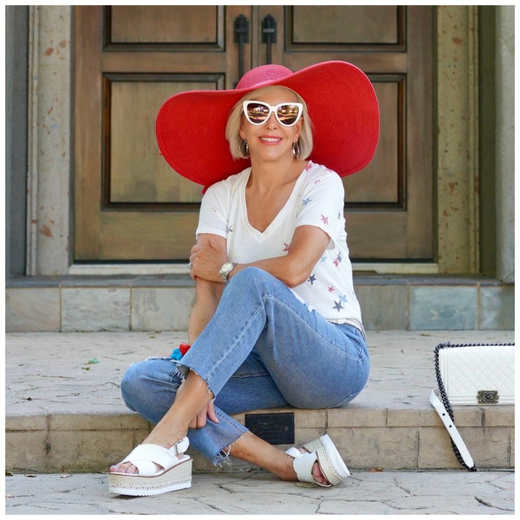 sheree of the SheSheShow sitting in front of house wearing ripped jeans and white star tee shirt and red hat