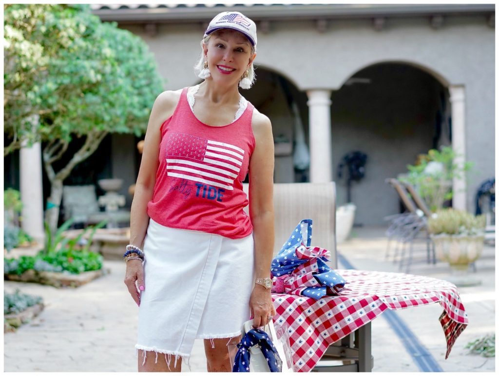 Sheree of the SheSheShow standing outside decorating for the 4th of july wearing white denim skirt and red flag t shirt